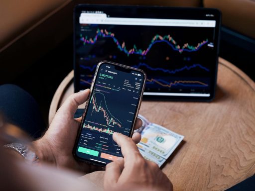 Close-up of a person trading stocks using a smartphone and a tablet.