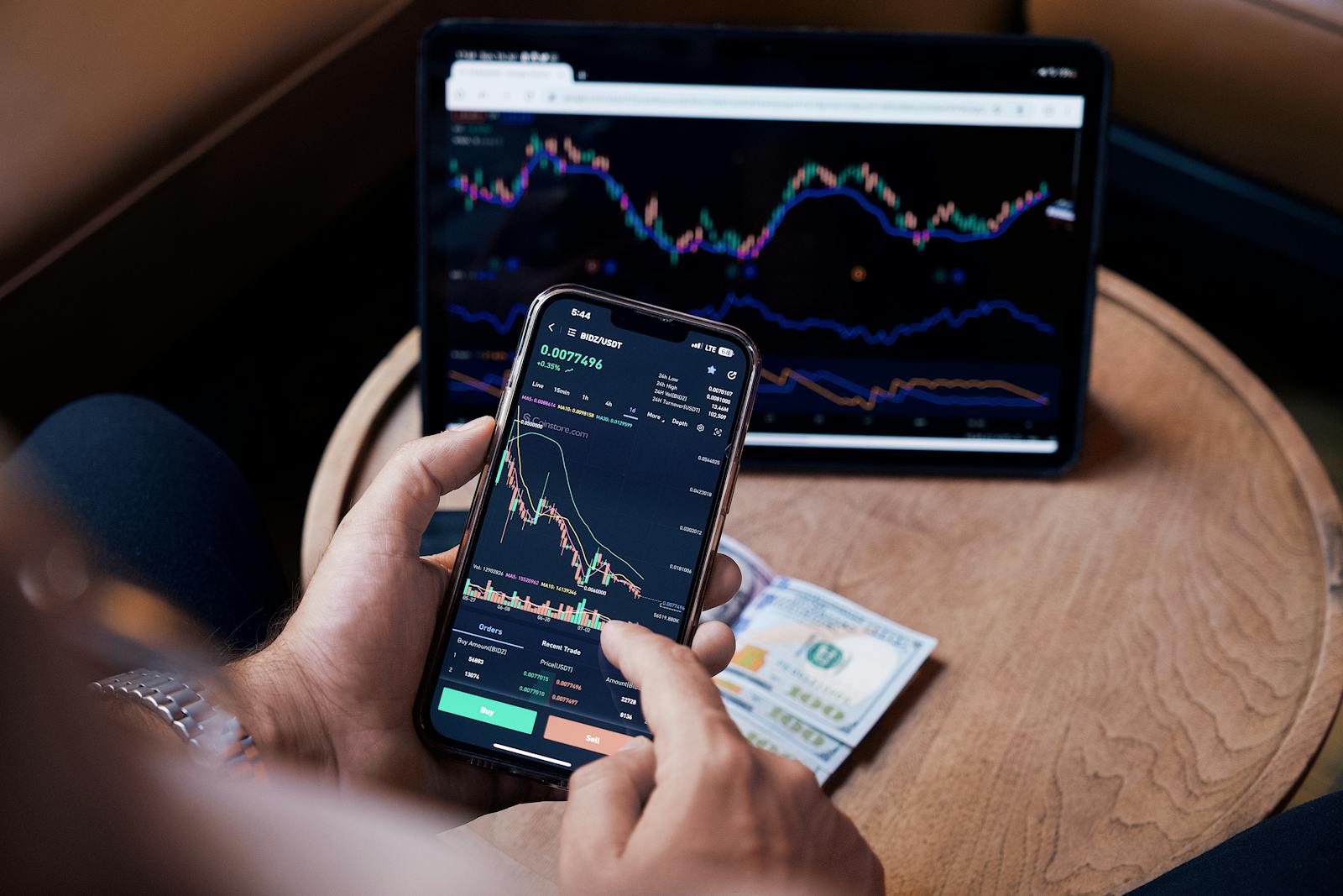 Close-up of a person trading stocks using a smartphone and a tablet.