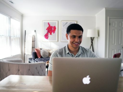 man in gray hoodie sitting on chair in front of silver macbook