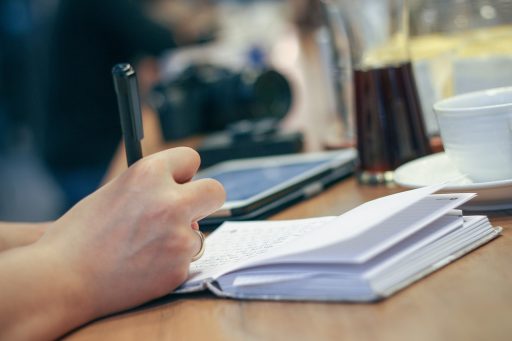 Persoon luistert naar podcast en maakt aantekeningen in notitieboek